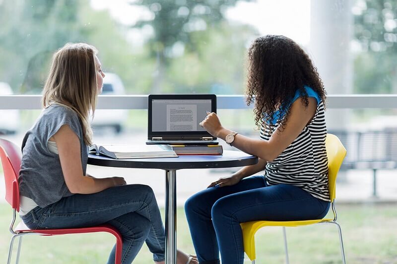 Two women chatting over a presentation on a laptop at a table